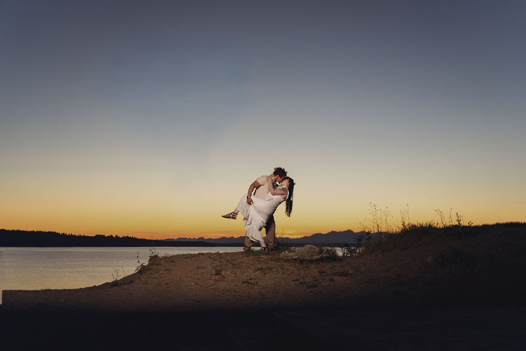 Partner dipping his fiancee for a kiss on a bluff above the water at twilight at Chambers Bay near Tacoma. engagement session worth it PNW