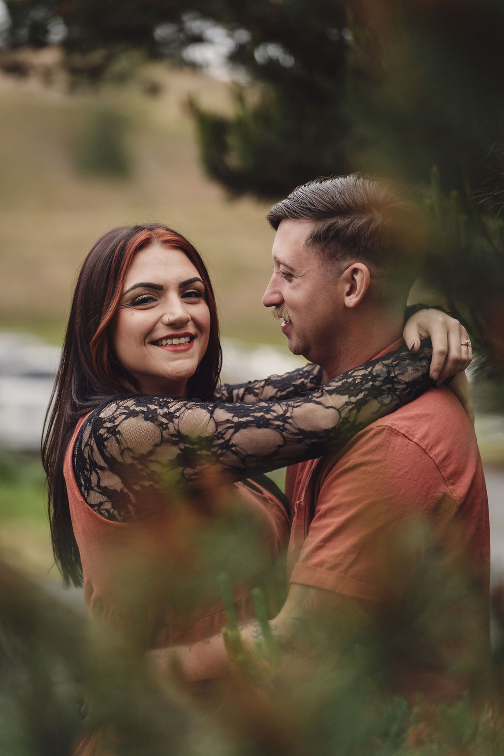 Engaged couple laughing together in a close embrace among the pine trees at Chambers Bay near Tacoma. Chambers Bay engagement photos Tacoma