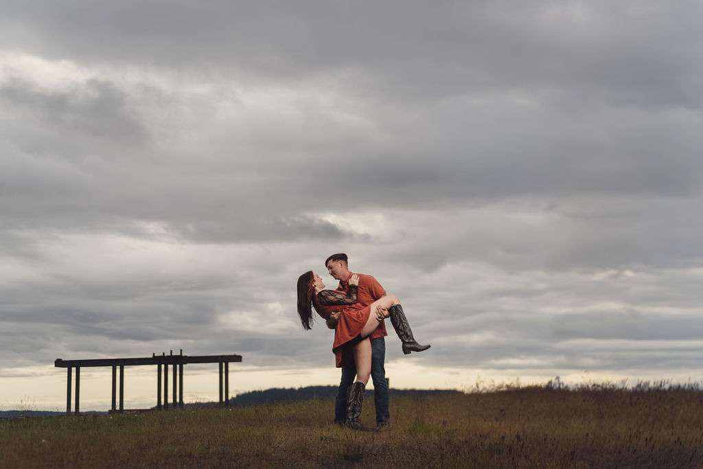 Partner dipping his fiancee in an open meadow at Chambers Bay under a dramatic cloudy sky near Tacoma