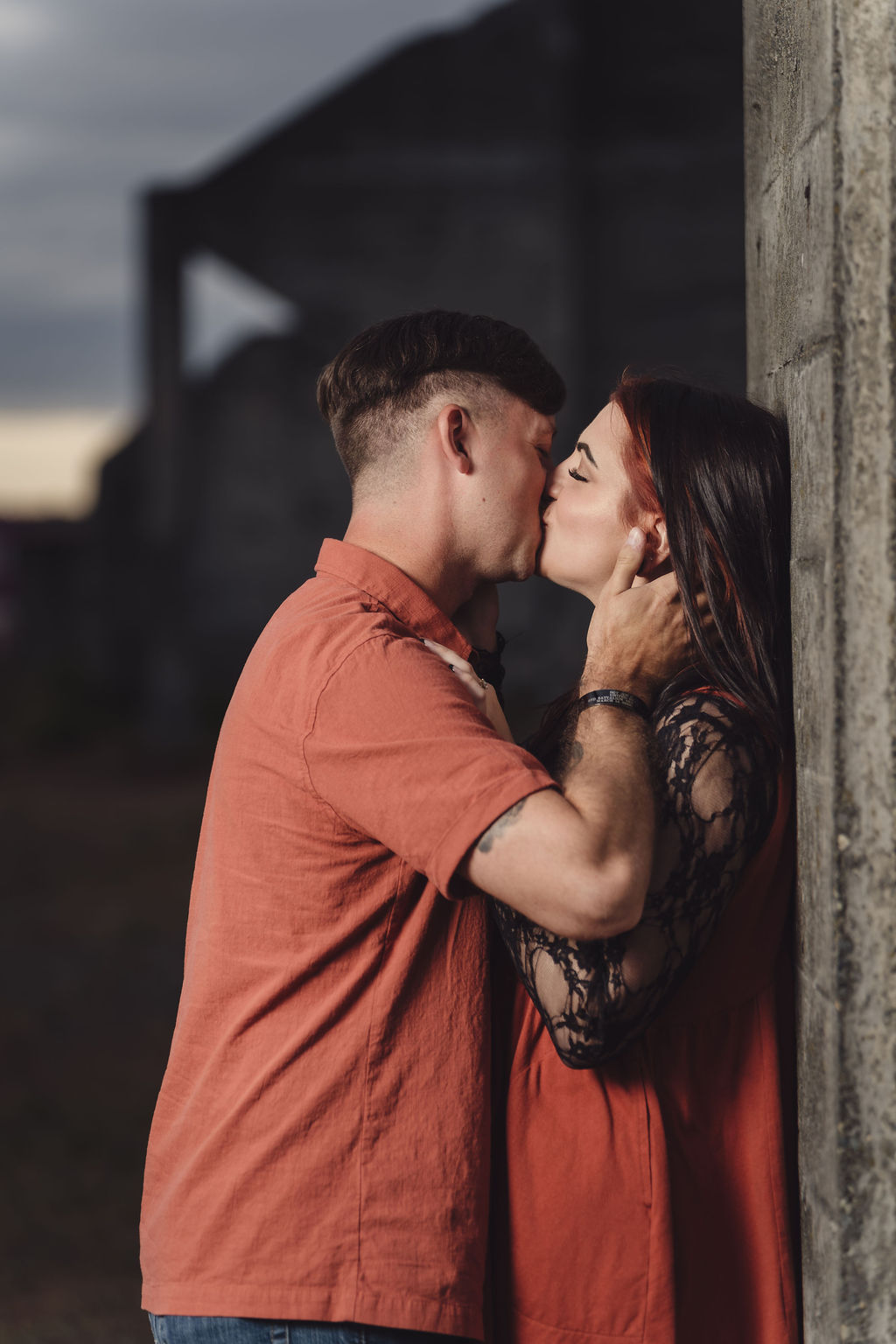 Engaged couple sharing a kiss while leaning against a concrete column at Chambers Bay near Tacoma at dusk