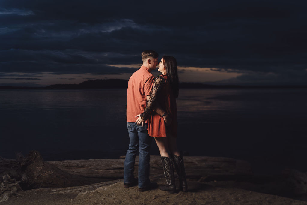 Engaged couple forehead to forehead on a driftwood beach above the water at Chambers Bay near Tacoma at dusk