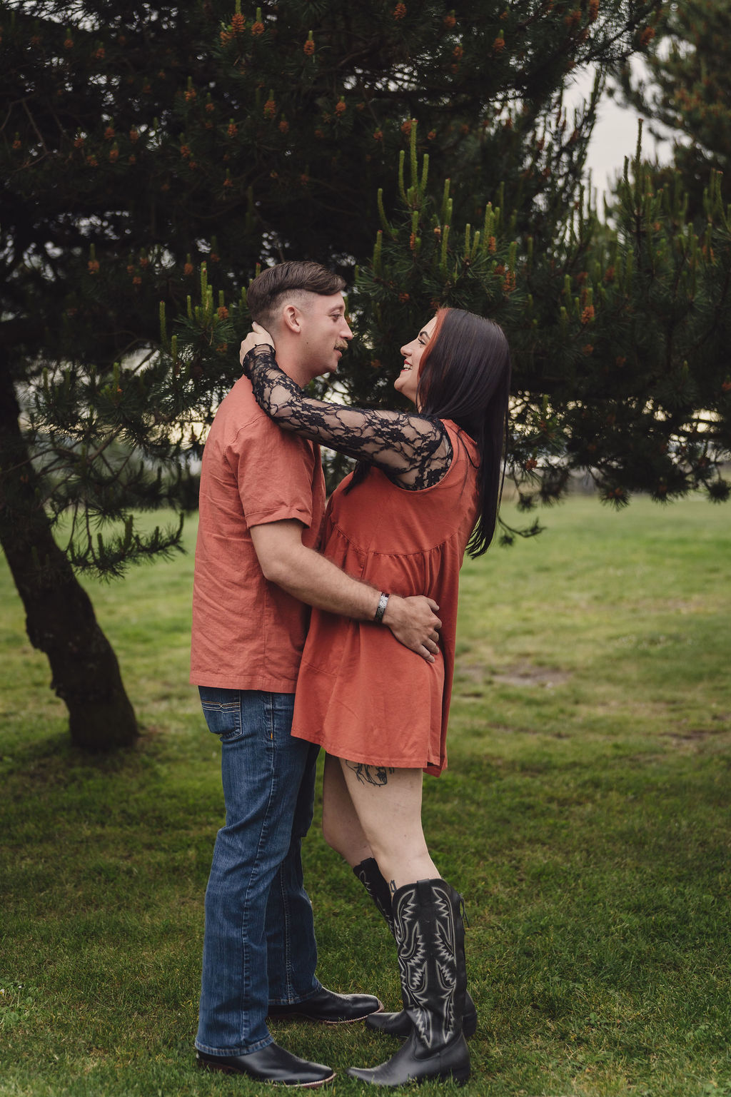 Engaged couple in coordinated autumn outfits embracing in front of a pine tree at Chambers Bay near Tacoma