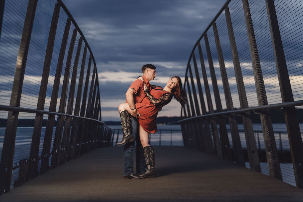 Partner dipping his fiancee on the boardwalk pier over the water at Chambers Bay at blue hour near Tacoma