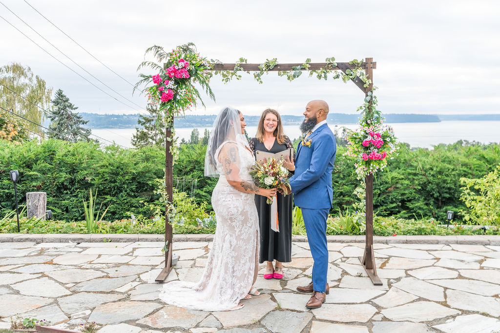 Bride and groom exchanging vows under a floral arch with a Puget Sound view at Damian's Venue in Tacoma