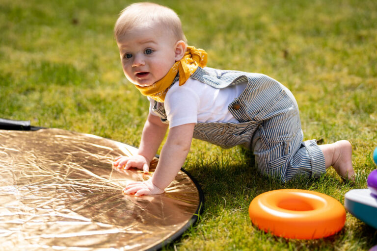 Baby in striped overalls crawling across the grass during an outdoor spring family session in Kitsap County