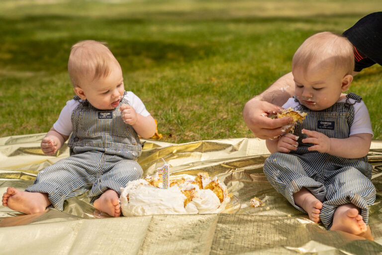 Dad hand feeding cake to his baby during an outdoor first birthday cake smash family session in Kitsap County