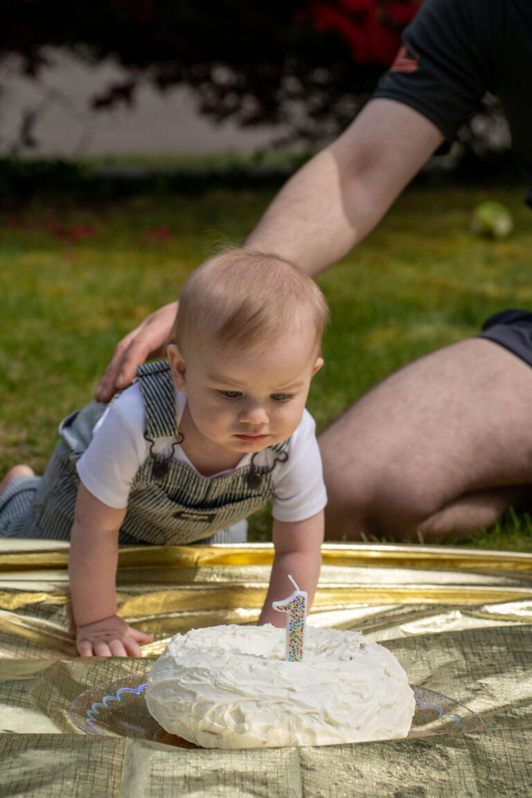Baby crawling toward a white first birthday cake with a number one candle at a Kitsap County cake smash