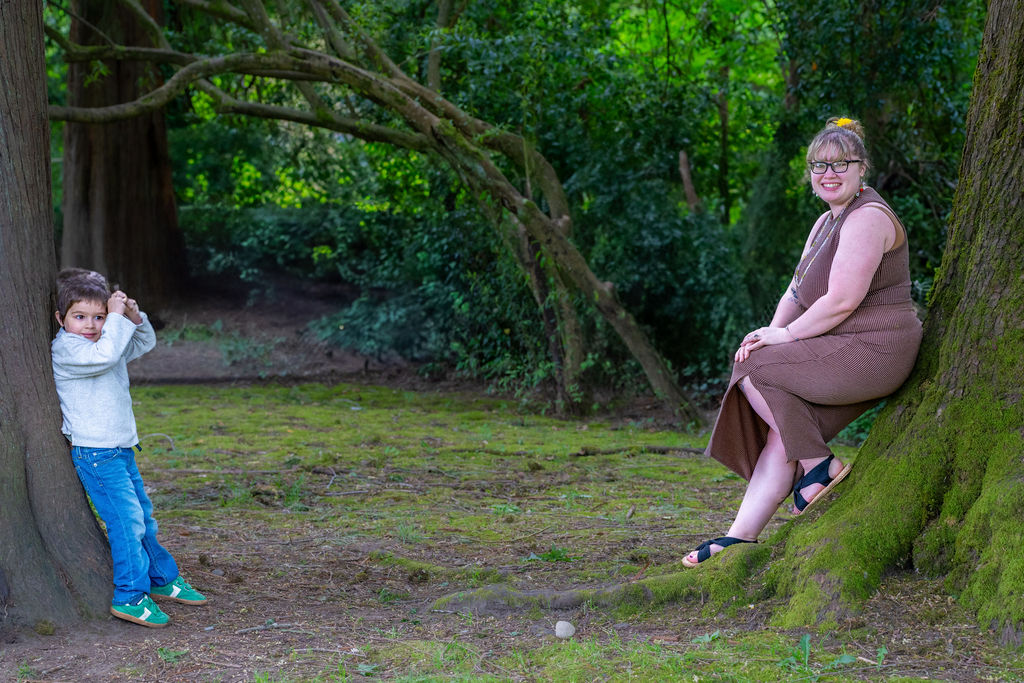 Young boy peeking around a tree while his mother rests nearby at a Kitsap County park