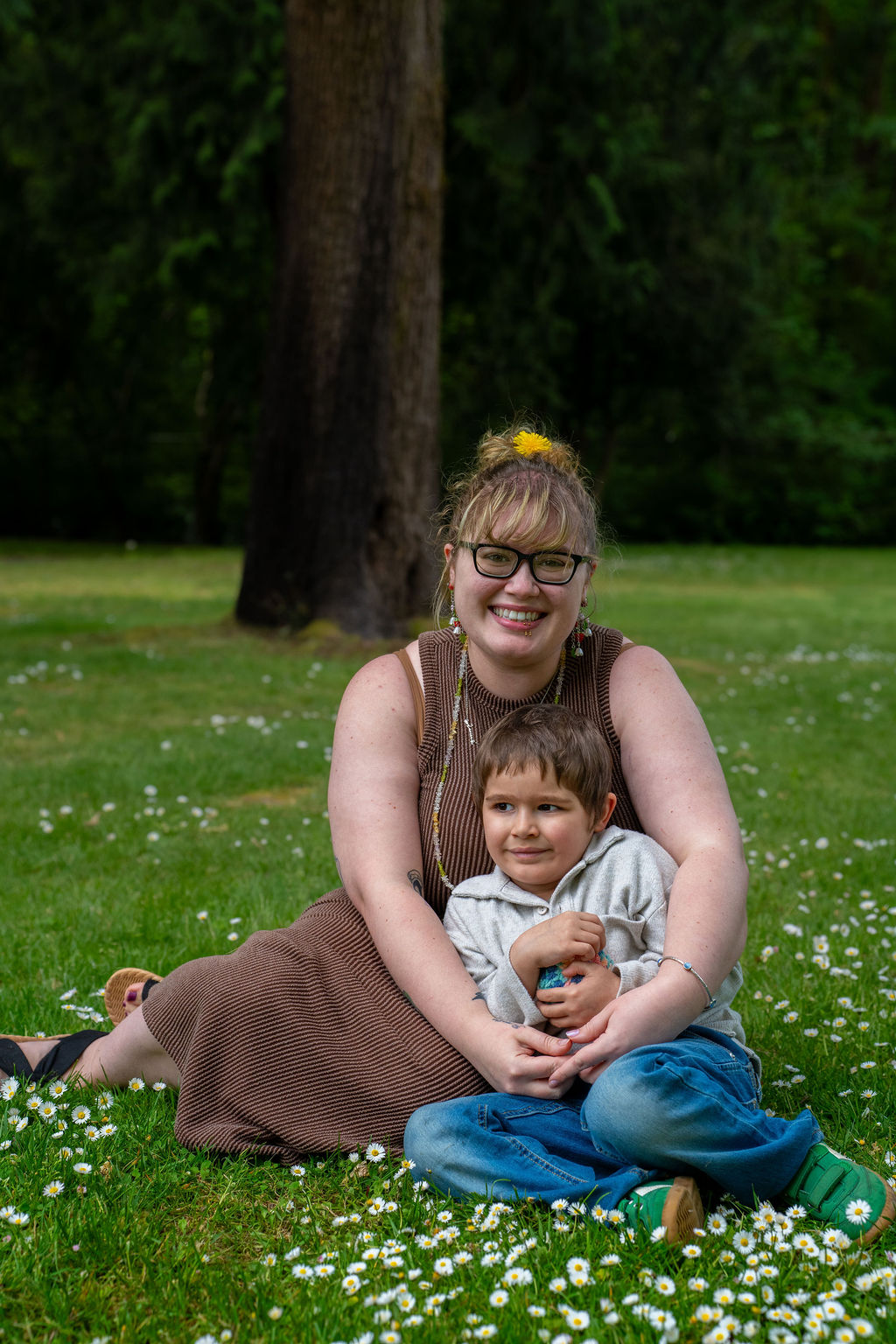 Family photo session with a mother and her son sitting in a daisy filled lawn at a park in Kitsap County, Washington
