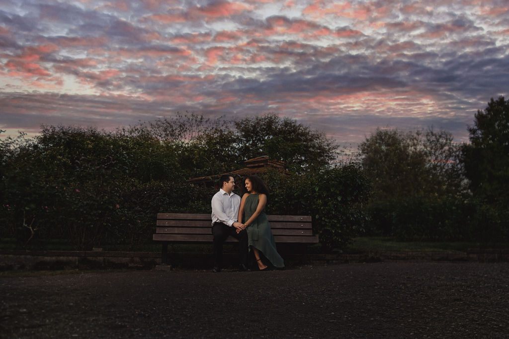 RJ and Maya sitting on a bench during sunset at Point Defiance Park for their Tacoma engagement session