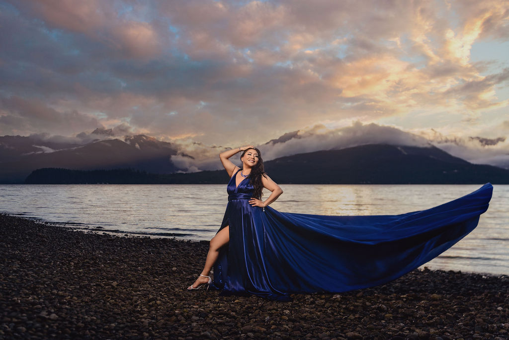 Woman in a royal blue gown with a sweeping train on the rocky beach with the Olympic Mountains and Hood Canal behind her at Scenic Beach State Park near Seabeck at sunset