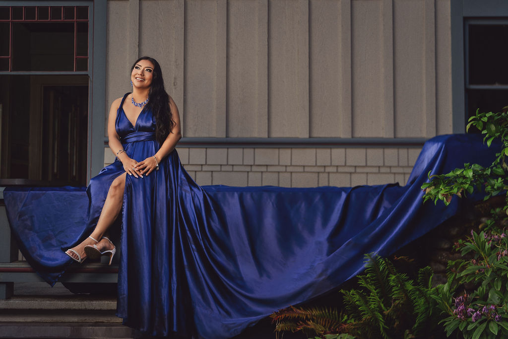 Woman in a royal blue gown with a flowing train seated by a historic building at Scenic Beach State Park near Seabeck