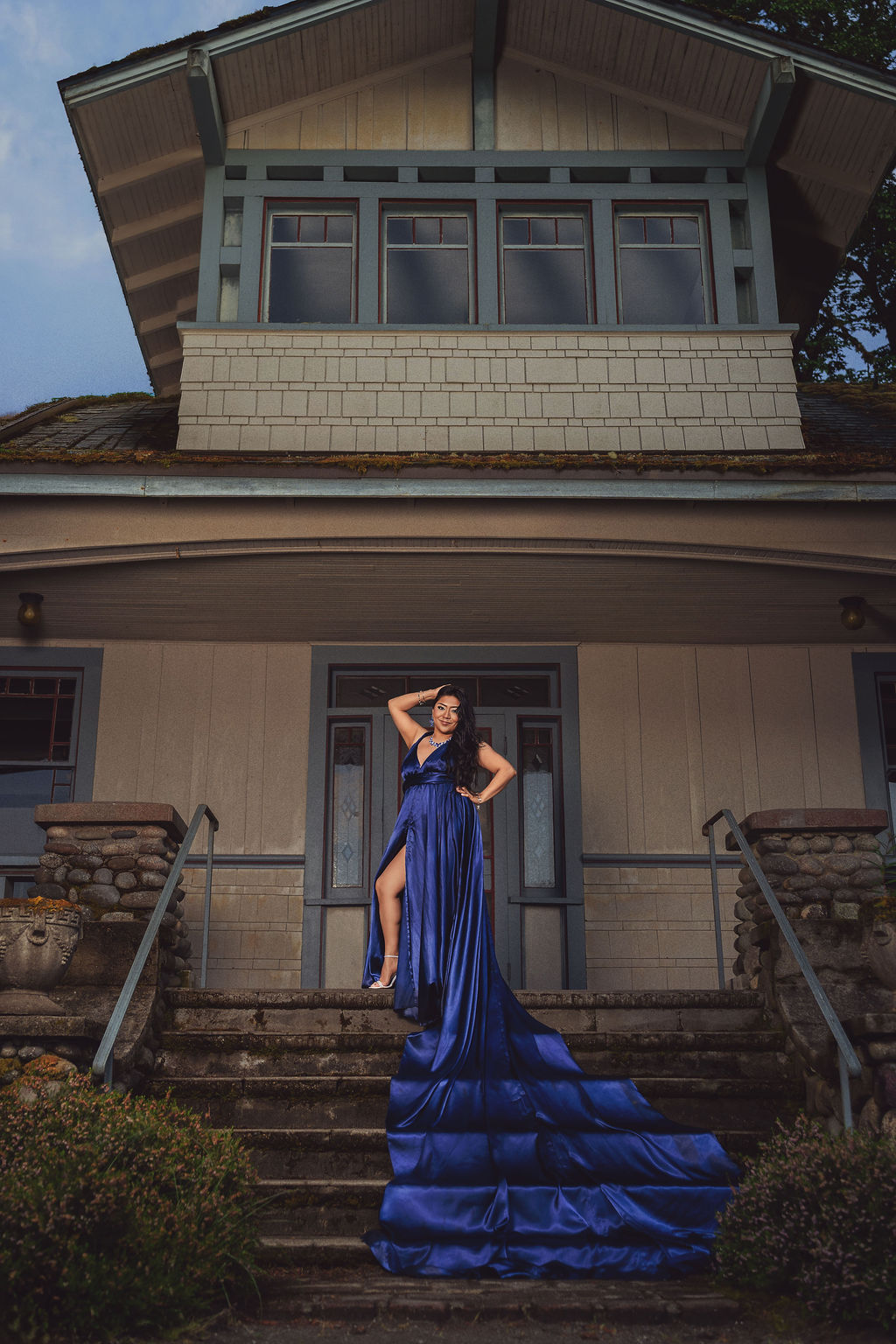 Woman in a royal blue gown with a long train cascading down the steps of the historic lodge at Scenic Beach State Park near Seabeck