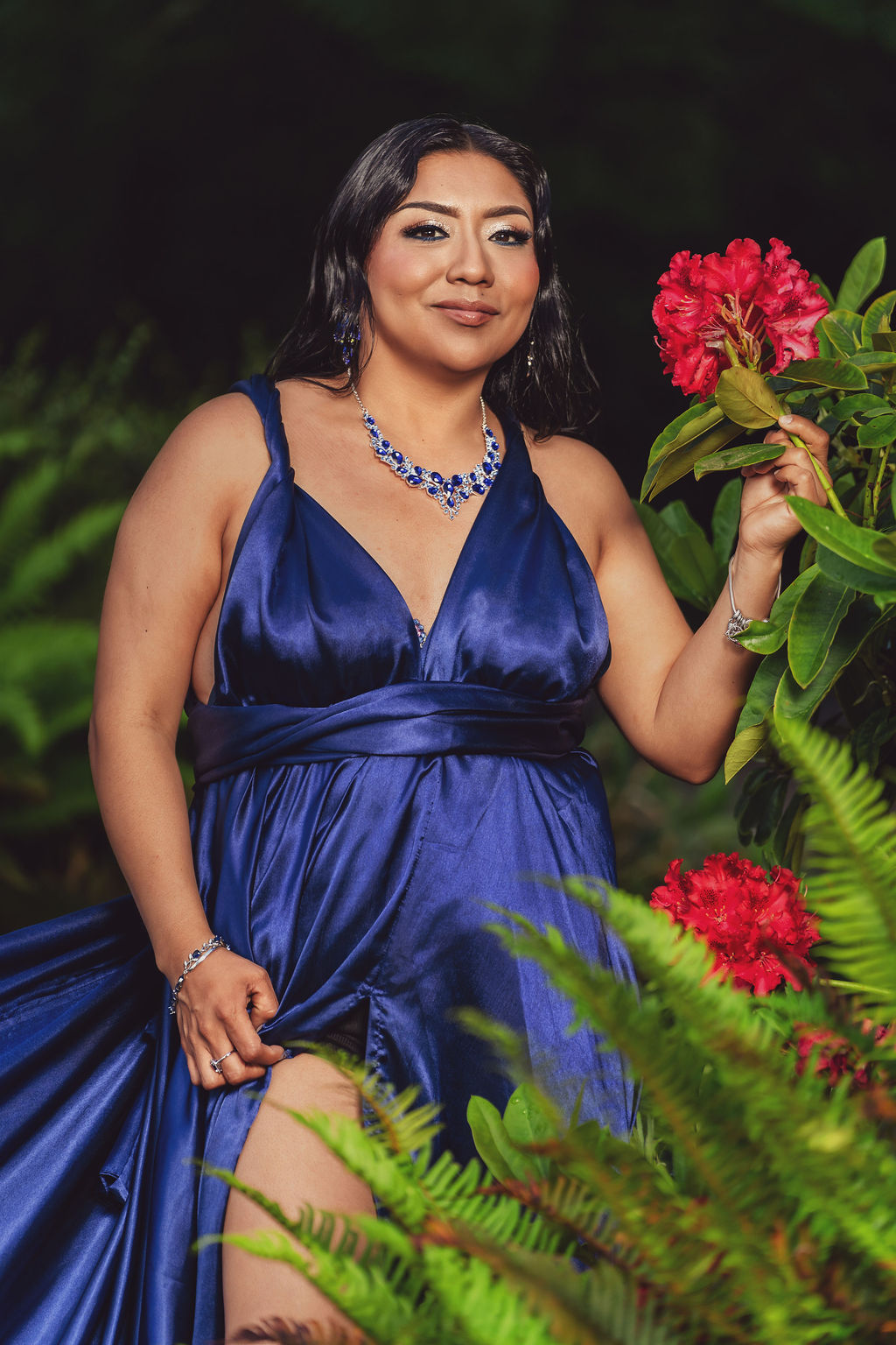 Beauty portrait of a woman in a royal blue gown holding red rhododendron blooms surrounded by ferns at Scenic Beach State Park near Seabeck