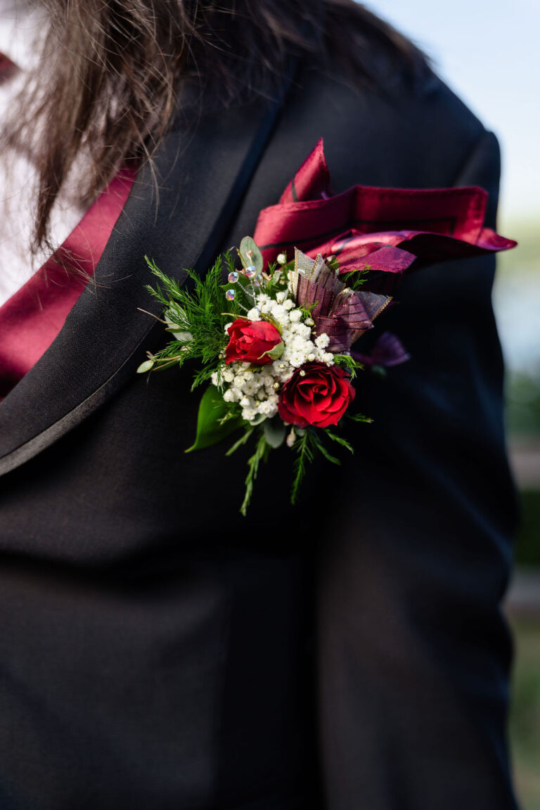 Close up of a red rose boutonniere on a black prom suit lapel with a burgundy pocket square, Kitsap prom details
