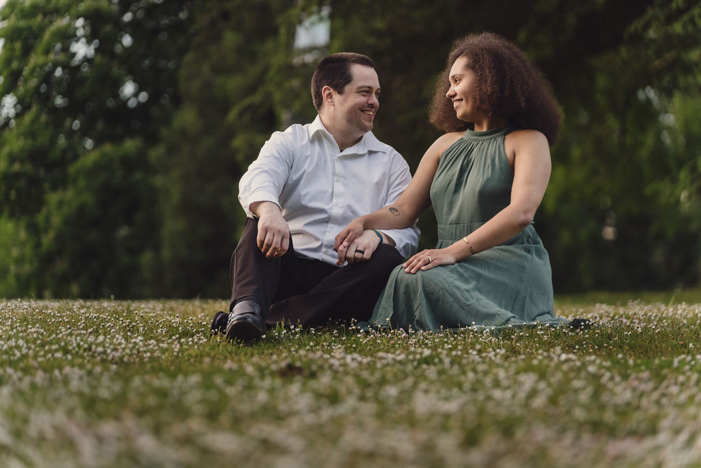 RJ and Maya sitting together in the grass and laughing during their Tacoma engagement photos
