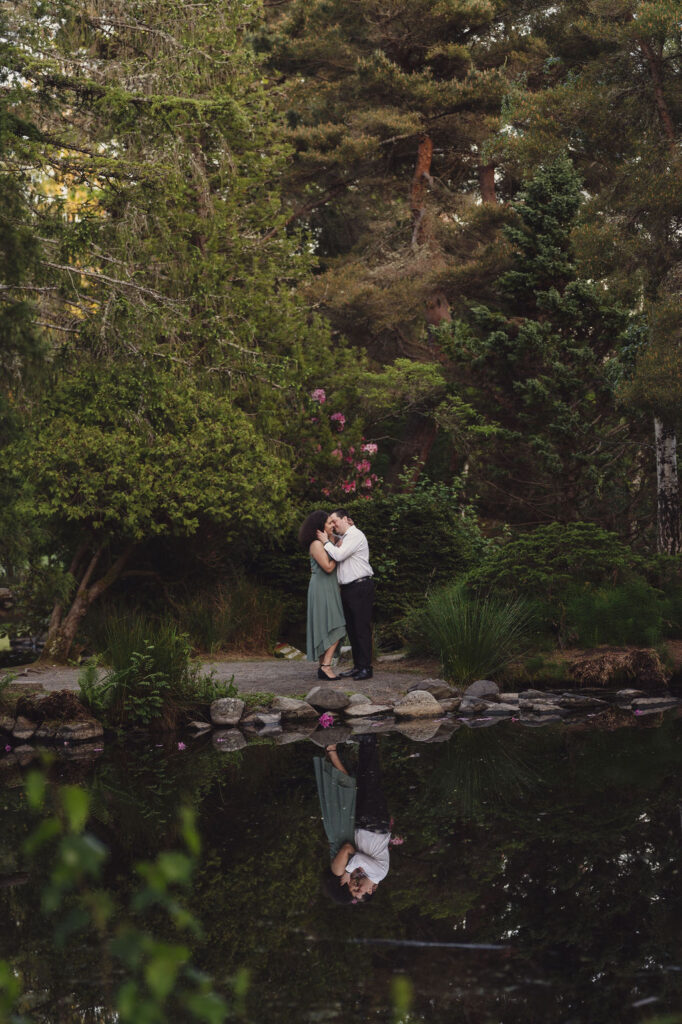 RJ and Maya sharing a romantic moment near the pond with their reflection in the water at Point Defiance Park