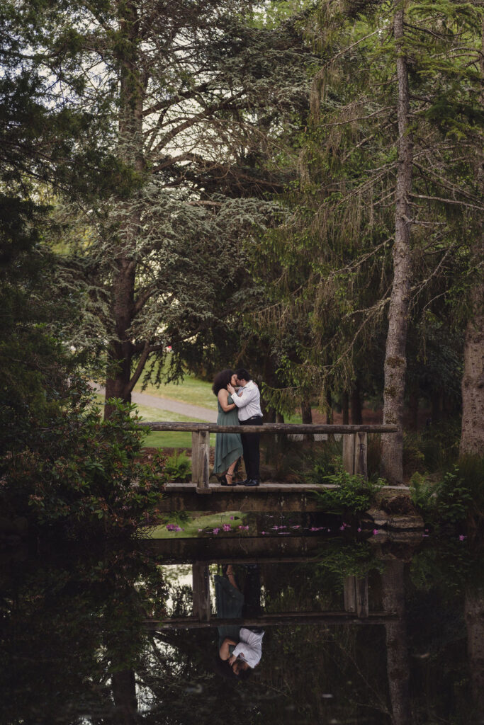 RJ and Maya standing together on a bridge with their reflection in the pond at Point Defiance Park