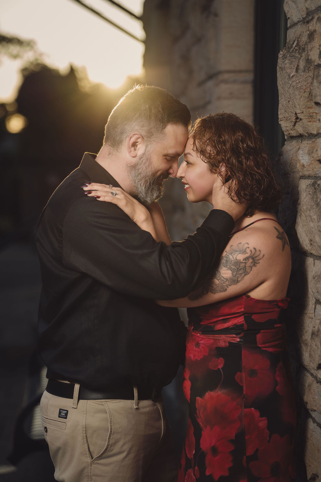 Engaged couple forehead to forehead against the historic brick wall of Stadium High School in Tacoma with golden hour sun flaring behind them. Stadium High School engagement photos Tacoma