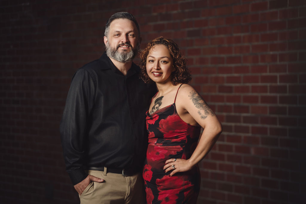 Engaged couple posing close together against a moody red brick wall during a Tacoma engagement session