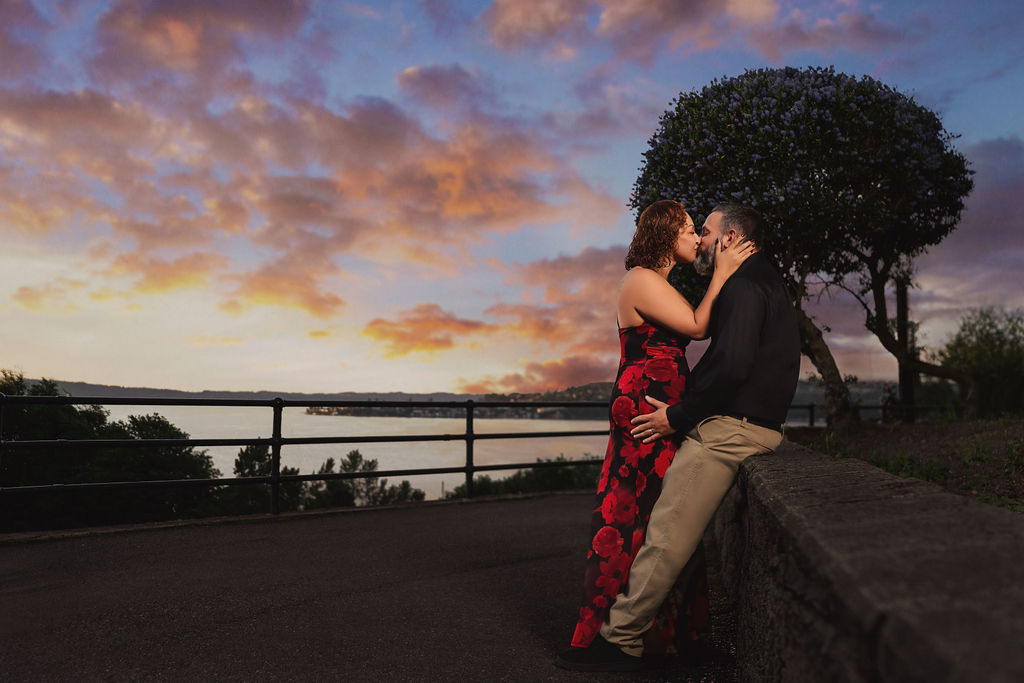 Engaged couple kissing under a vivid pink and purple sunset sky overlooking Commencement Bay in Tacoma