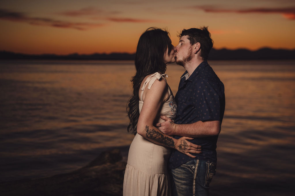 Engaged couple sharing a kiss by the water at sunset at Chambers Bay near Tacoma