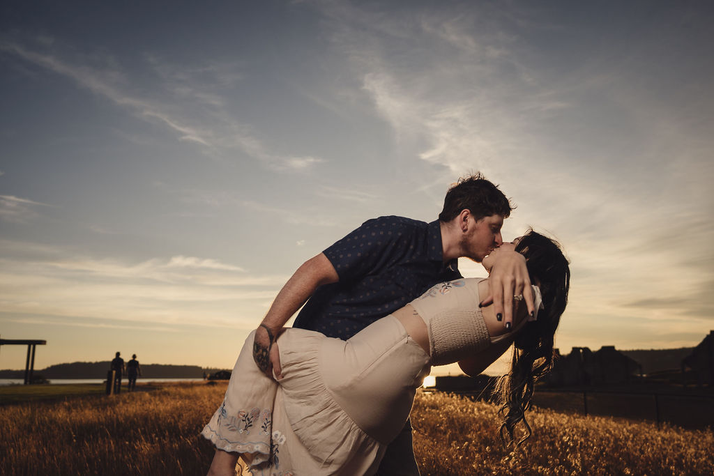 Engaged couple in a dip kiss with sun flare in a golden field at Chambers Bay near Tacoma