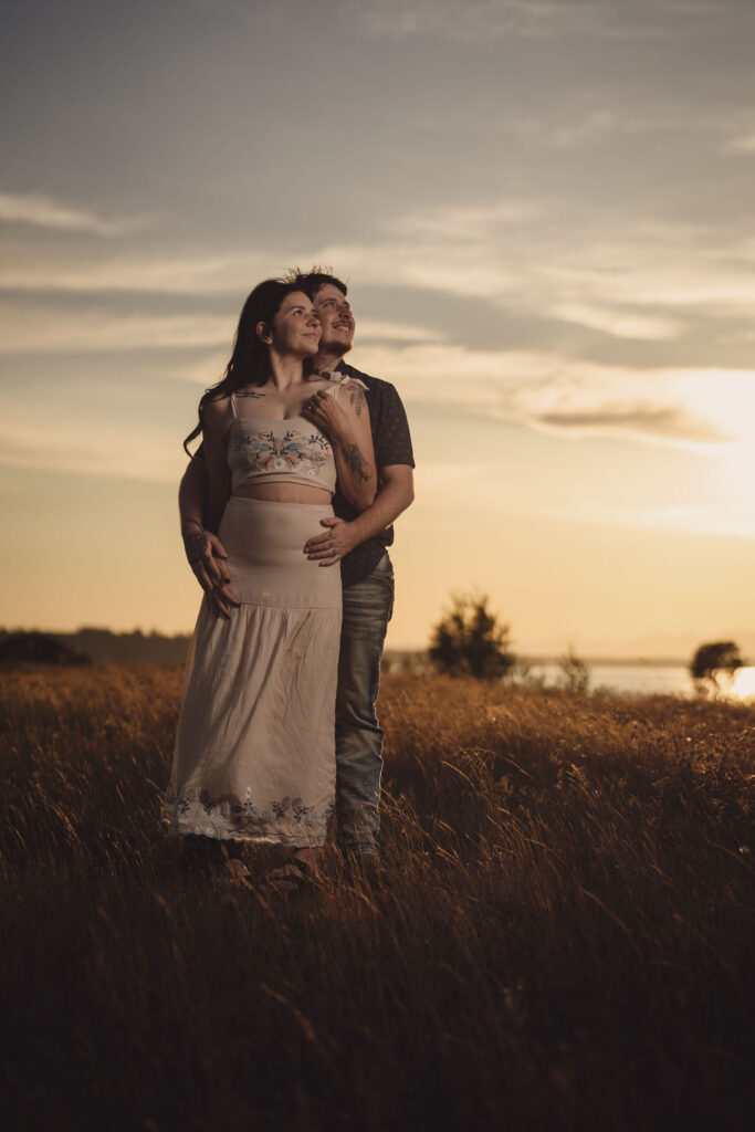 Engaged couple embracing in a golden field at sunset at Chambers Bay near Tacoma