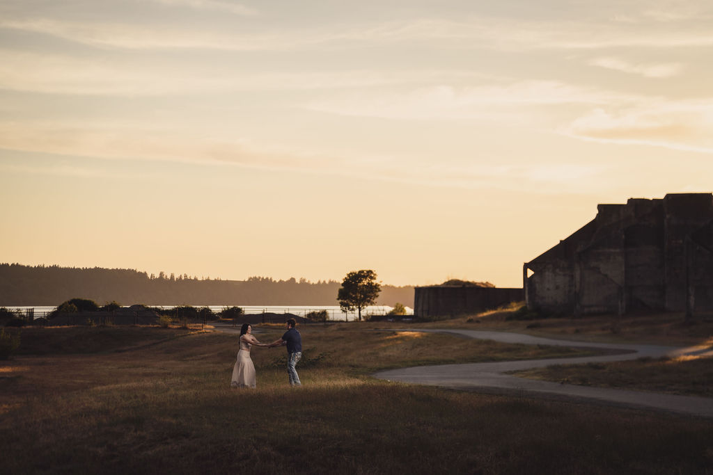Engaged couple embracing under a wide sunset sky at Chambers Bay near Tacoma