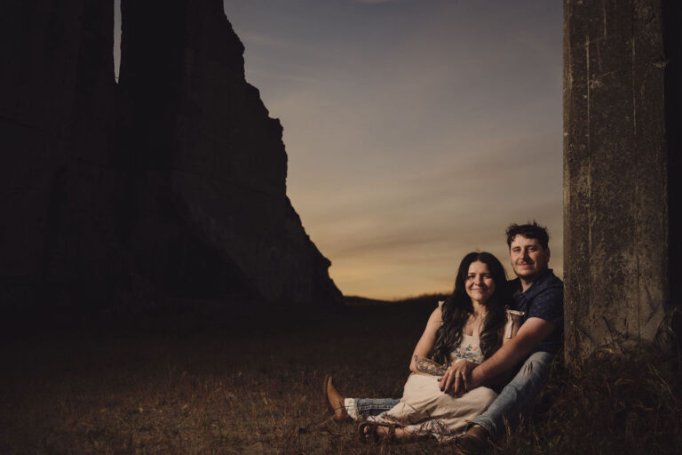 Engaged couple seated against the concrete ruins at dusk at Chambers Bay near Tacoma