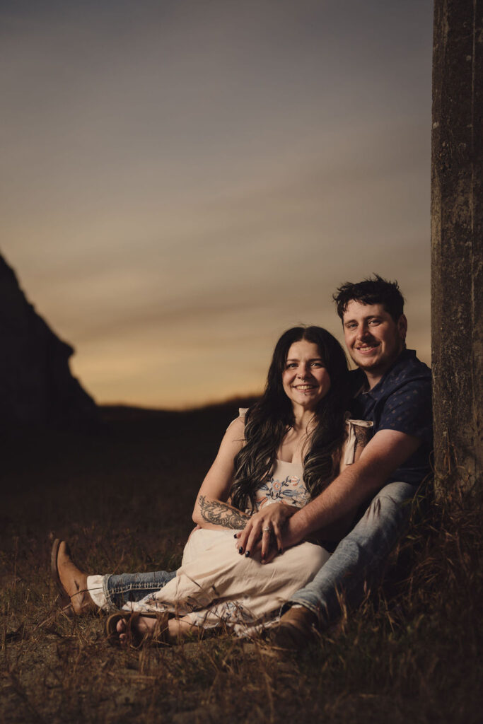 Engaged couple sitting close in a golden grass field at dusk at Chambers Bay in University Place