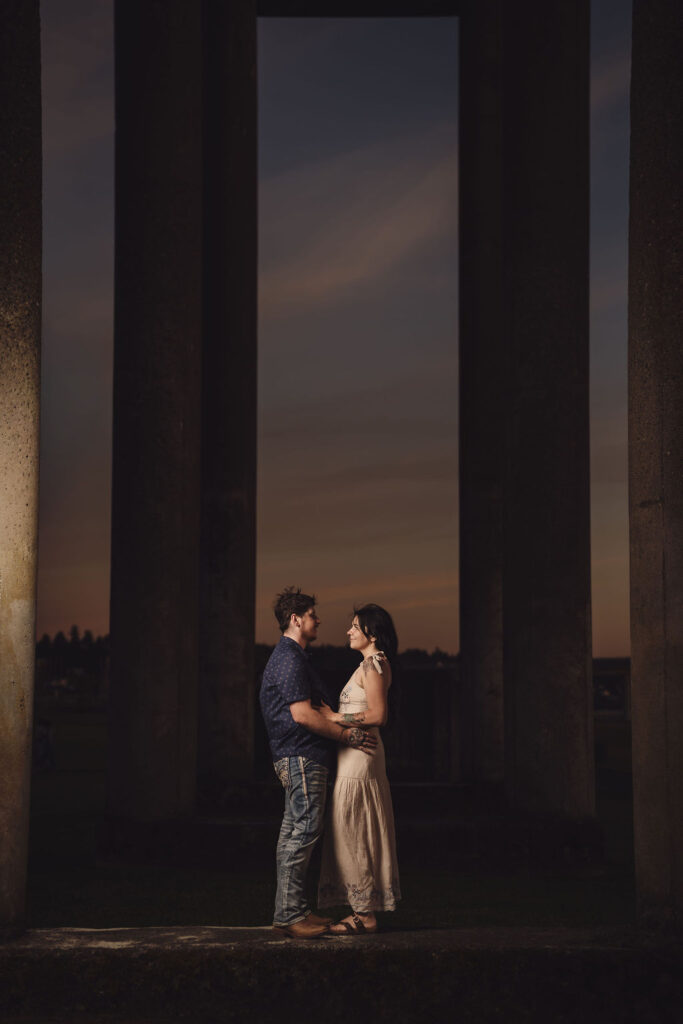 Engaged couple embracing framed between the towering concrete pillars at Chambers Bay in University Place