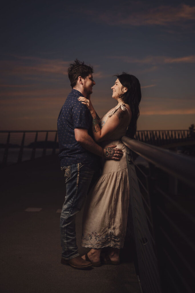 Engaged couple embracing at the boardwalk railing at sunset at Chambers Bay near Tacoma