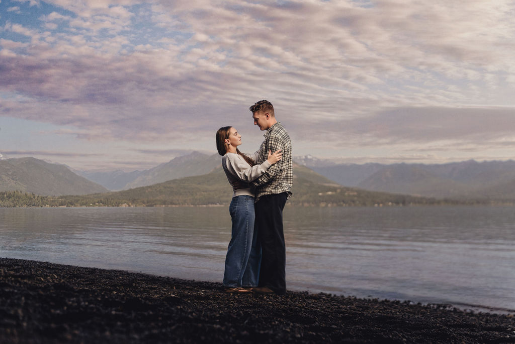 Engaged couple embracing on the pebble beach at Scenic Beach State Park with Hood Canal and the Olympic Mountains behind them