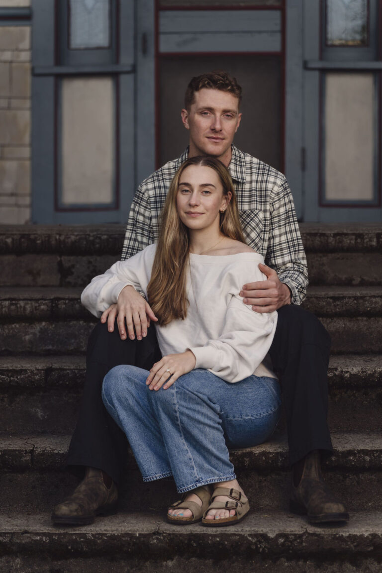 Bride to be sitting in her partner's lap on the historic house steps at Scenic Beach State Park in Seabeck