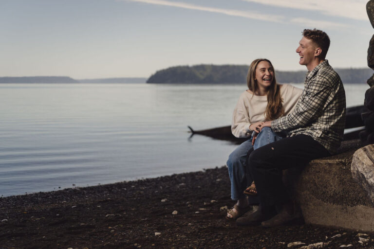 Couple laughing while seated on driftwood along Hood Canal at Scenic Beach State Park
