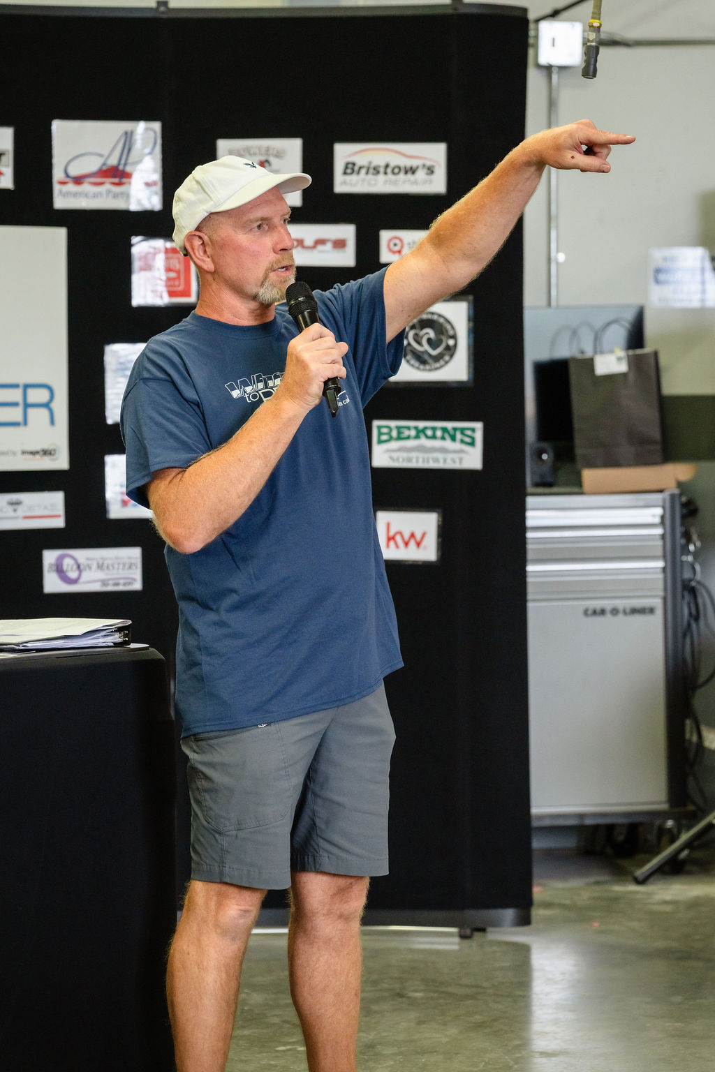 An organizer speaks into a microphone in front of the sponsor logo backdrop