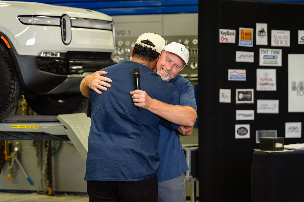 Two organizers share a hug beside the lifted truck at the Tacoma charity event