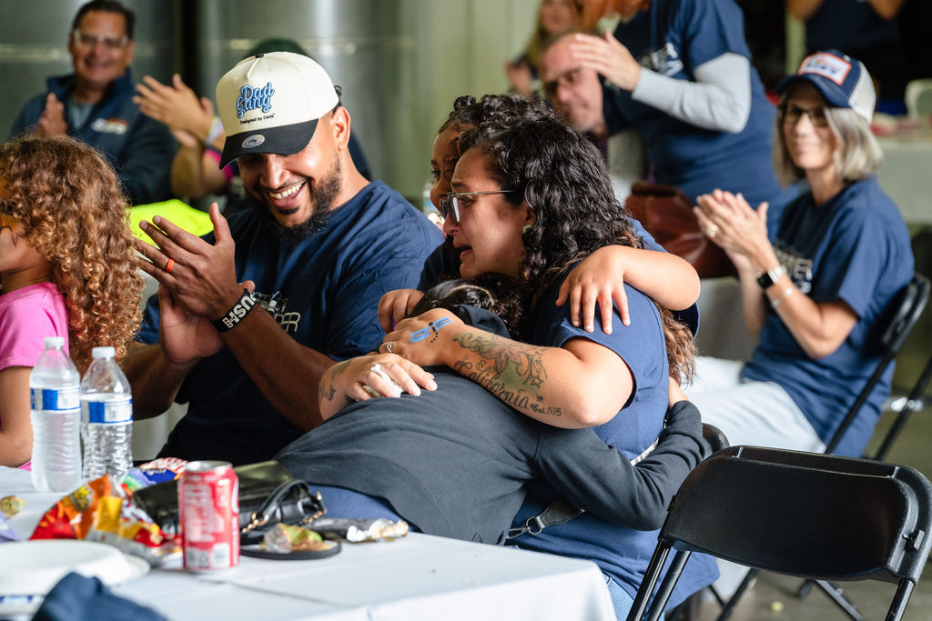 Local business owners applaud as the family embraces after learning they won the car