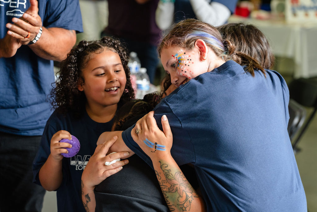 A smiling daughter beside relatives hugging during the Tacoma community car donation event