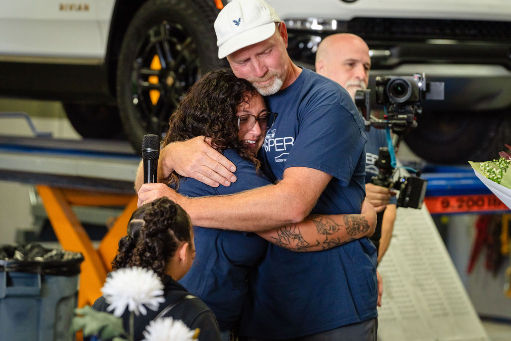 An organizer hugs the tearful recipient while a videographer records the Tacoma giveaway