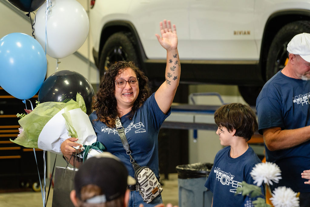 Mother waving and holding flowers at a Tacoma charity car giveaway celebration