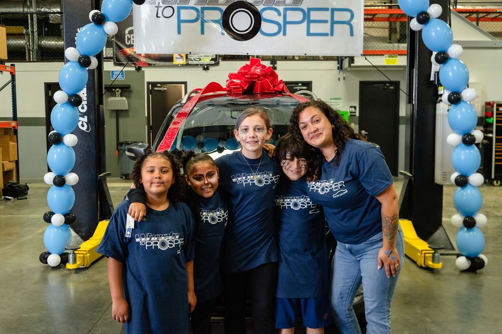 Family hugging under a balloon arch beside their new car at a community event