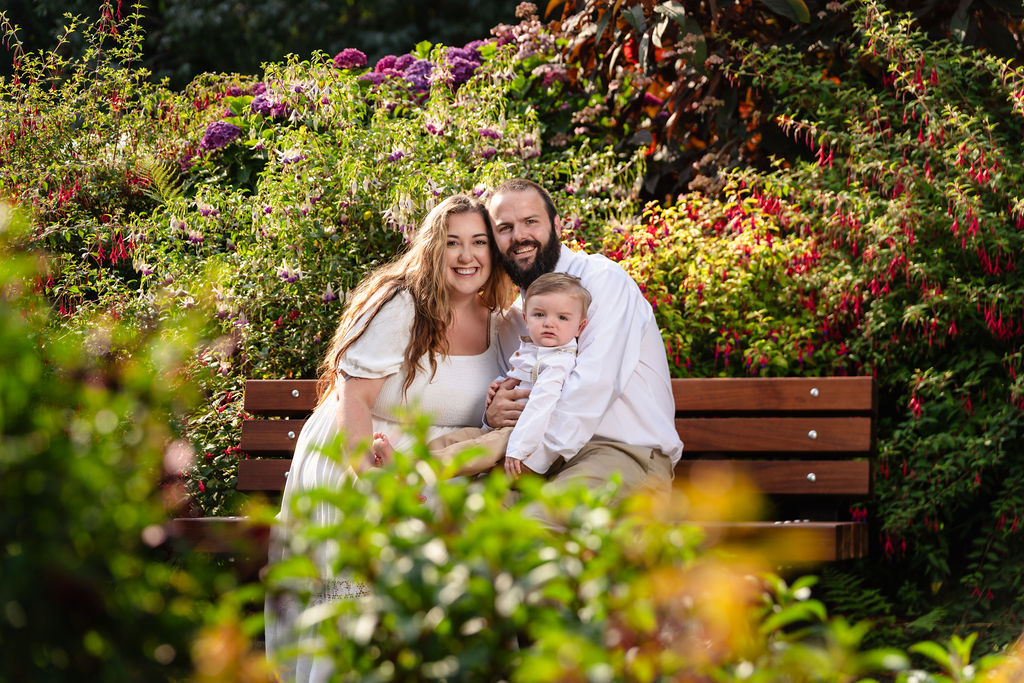 Family of three smiling on a garden bench at the Point Defiance Rose Garden in Tacoma