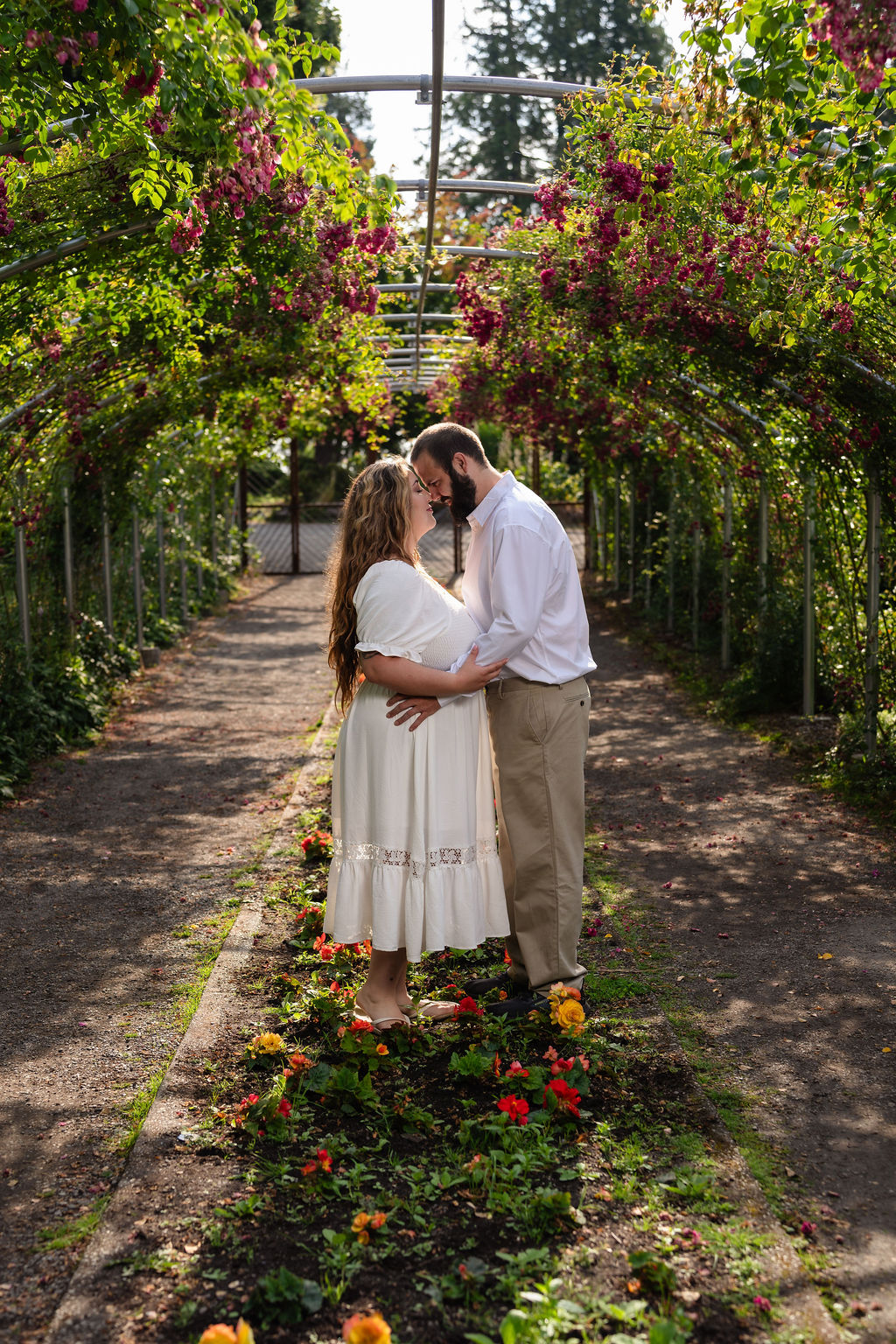 Engaged couple forehead to forehead in the sunlit rose archway at Point Defiance in Tacoma