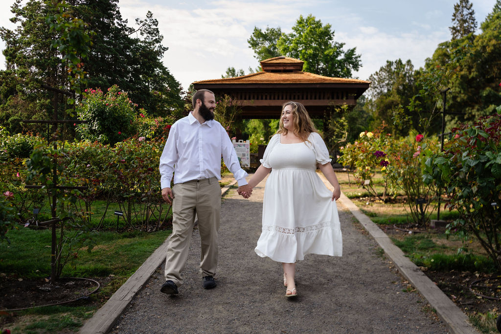 Engaged couple walking hand in hand toward the pagoda at the Point Defiance Rose Garden in Tacoma