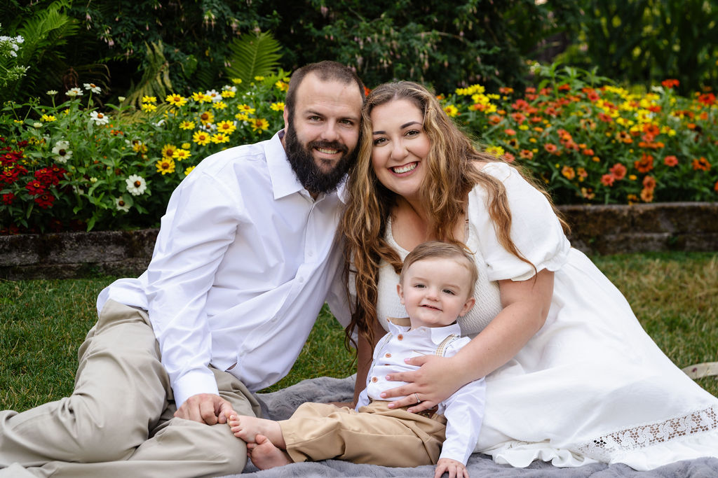 Parents and their baby son smiling on a picnic blanket at the Point Defiance Rose Garden in Tacoma