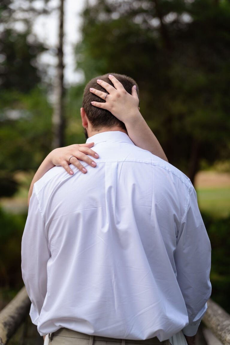 Engagement ring on her hand as she holds him close at Point Defiance in Tacoma Washington