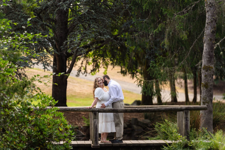 Engaged couple laughing nose to nose framed by evergreens at Point Defiance Park in Tacoma