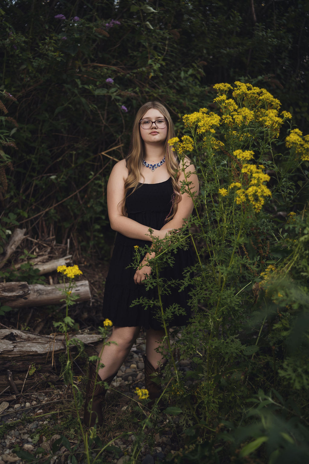 Senior girl in a black dress and cowboy boots standing beside tall yellow wildflowers at Belfair State Park